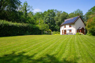 White two-storey house with brown shutters next to a wide grassy garden