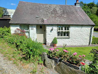 White washed cottage with path leading to front door. Lawn and mature flower bed