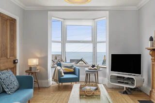 Living room with bay window, blue armchairs, TV and sea view