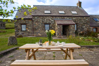 Outdoor picnic table with cups, teapot and flowers outside a stone house