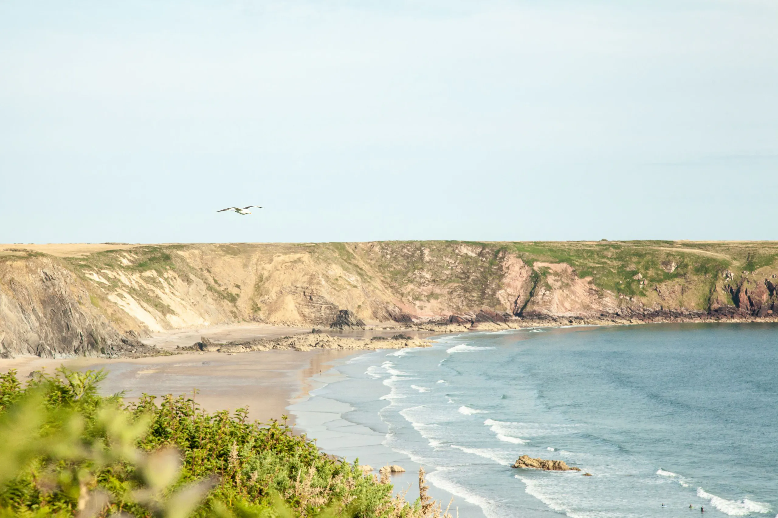 Sandy bay with small waves and cliffs under a pale sky