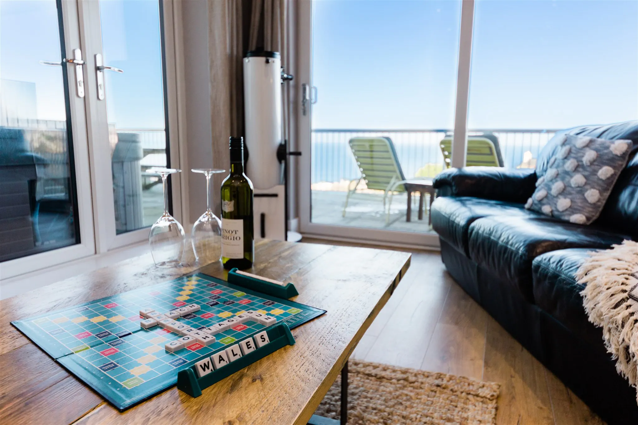 Scrabble board on a coffee table with wine bottle and glasses beside a sofa
