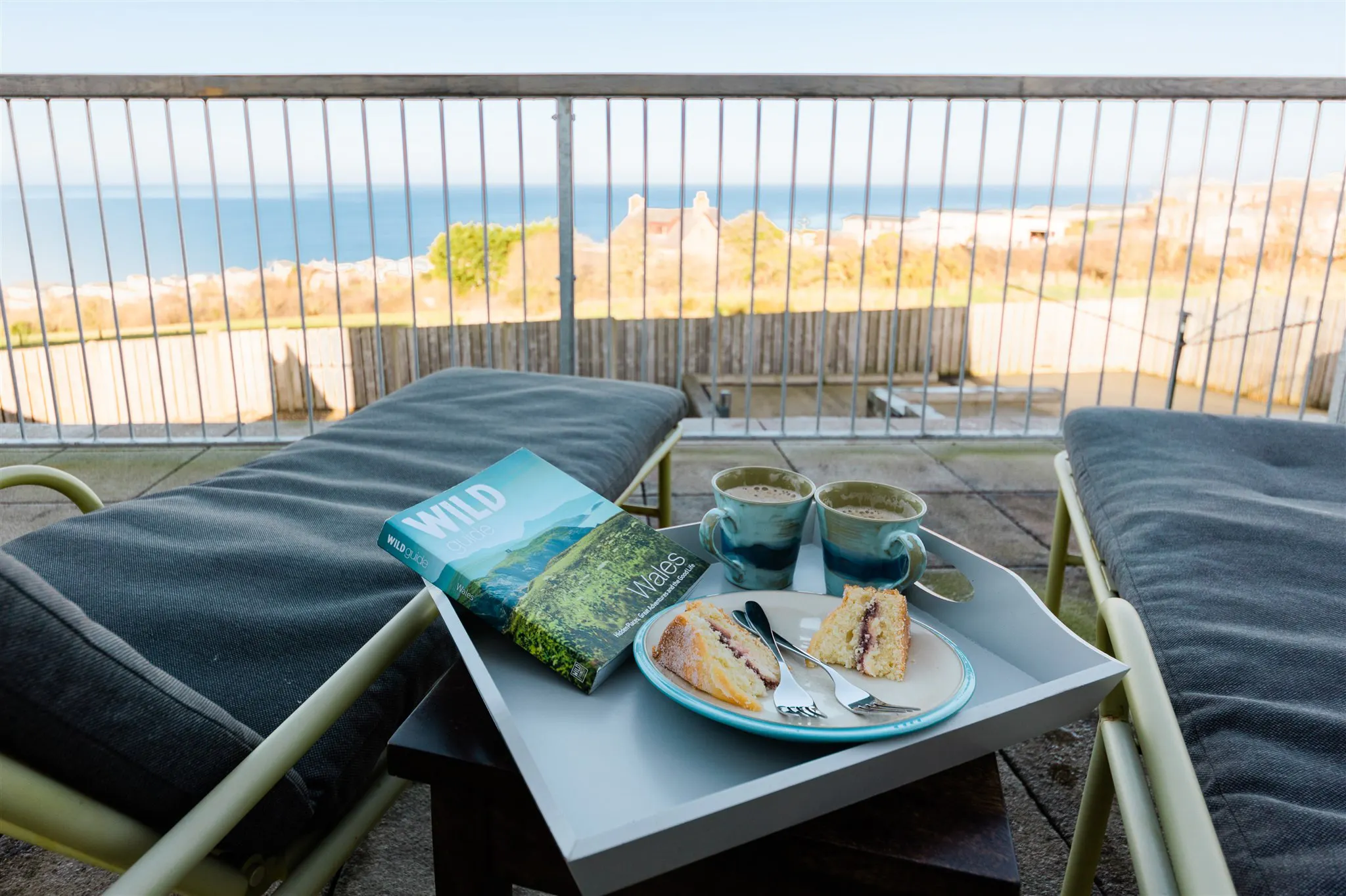 Balcony seating with two loungers and a tray of refreshments on a small table near the railing
