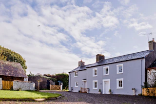 Grey house with slate roof and two chimneys, viewed from the driveway