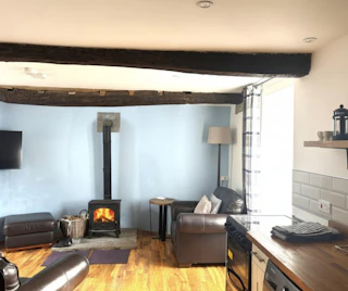 Living room with wood-burning stove, exposed beams, and leather seating