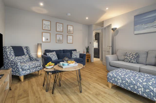 Living room with grey sofa, patterned armchair and footstool, and round coffee table with snacks