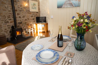 Round dining table set with plates, cutlery and wine bottle beside a vase of flowers