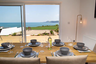 Dining table set with bowls and glasses beside sliding doors to a sea view