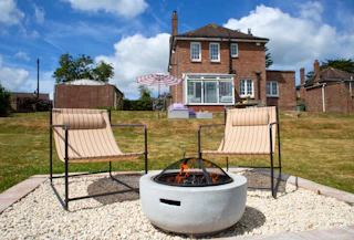 Garden seating area with two outdoor chairs and circular fire pit, lawn and brick home