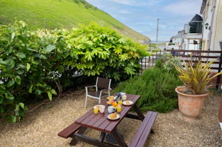 Breakfast spread on a wooden picnic table near potted plant and greenery