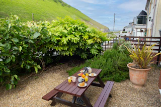 Picnic table with breakfast and drinks in a gravel garden beside houses