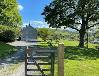 Gravel driveway and wooden gate in a rural garden with a house in the distance