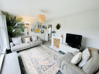 Dolwyn sitting room. Grey sofa and armchair. Patterned rug. TV on white cupboard
