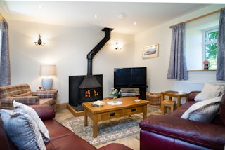 Living room in Towy Cottage, armchair, leather sofas, coffee tables around the logburner and TV