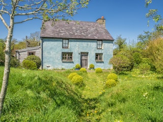 The outside of Ty Glas with trees and bushes and lawns